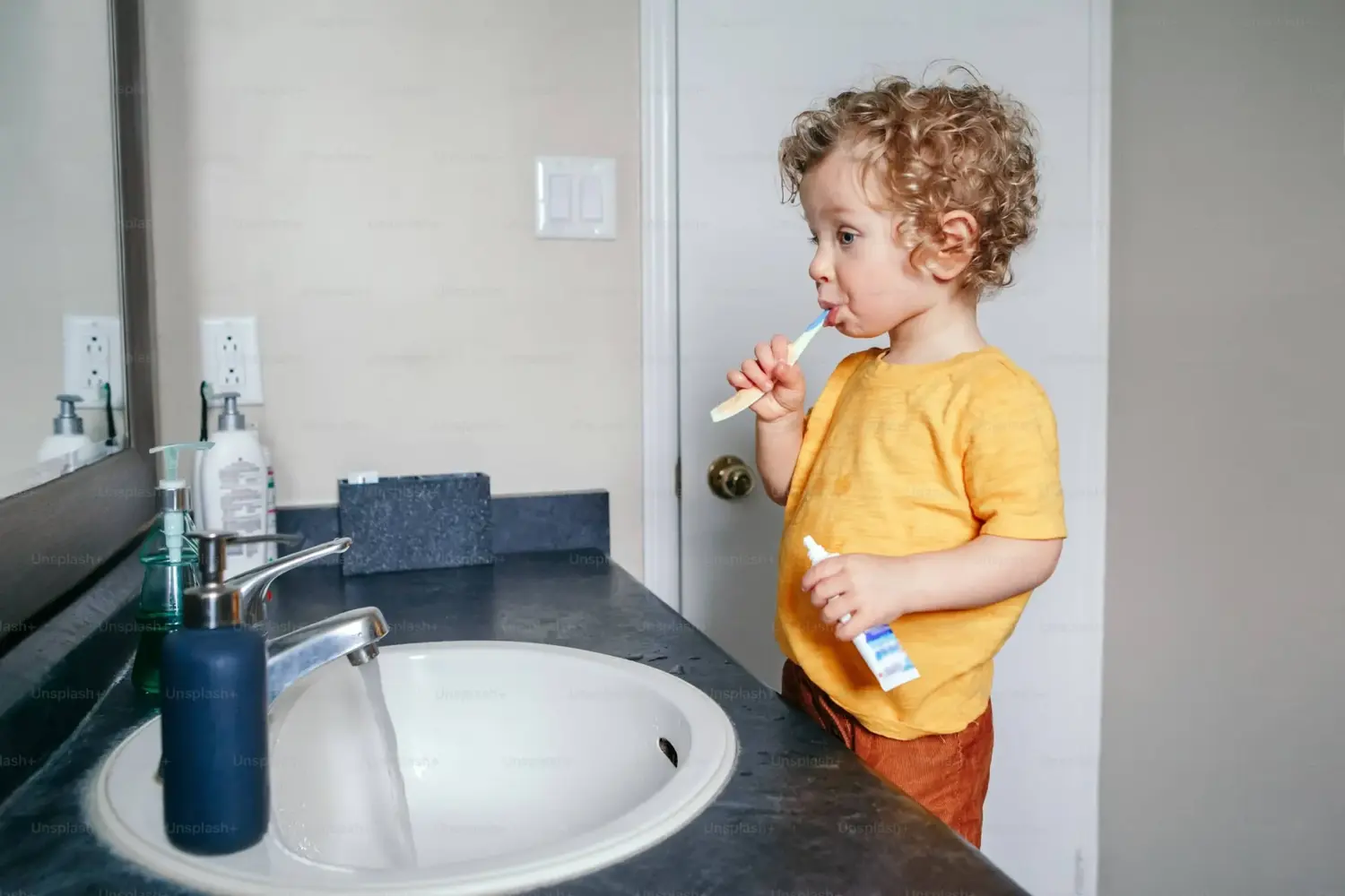 Jeune enfant se brossant les dents seul devant un lavabo de salle de bain.