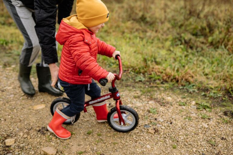 Enfant de 2 ans sur une draisienne rouge, les deux pieds posés à plat au sol