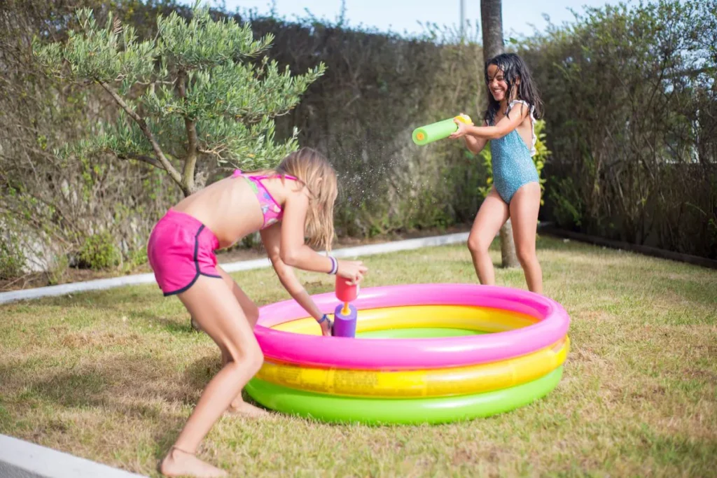 Deux fillettes qui s'amusent avec un jet d'eau dans une petite piscine gonflable