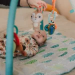 Bébé allongé sur un tapis d'éveil, attrapant les jouets suspendus à l'arche