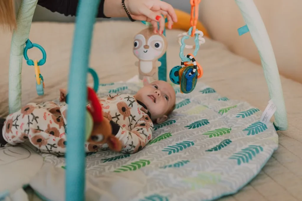 Bébé allongé sur un tapis d'éveil, attrapant les jouets suspendus à l'arche