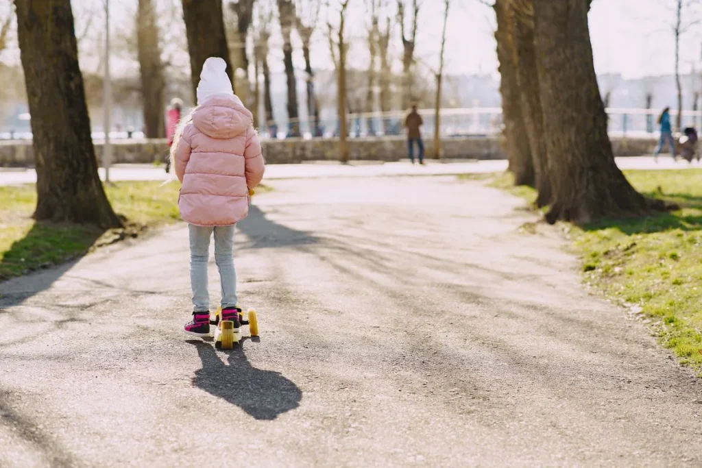 Petite fille de 3 ans sur sa trottinette dans un parc en automne