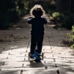 Enfant roulant en trottinette sur une allée de jardin ensoleillée