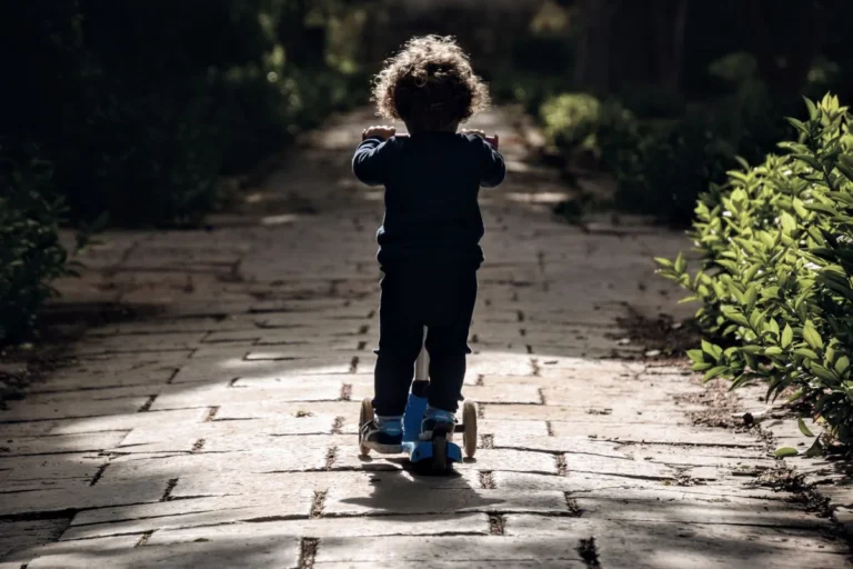 Enfant roulant en trottinette sur une allée de jardin ensoleillée