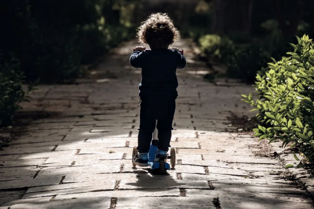 Enfant roulant en trottinette sur une allée de jardin ensoleillée