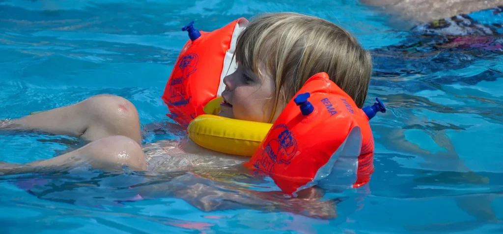 Enfant équipé de brassards et d’une bouée de cou dans une piscine